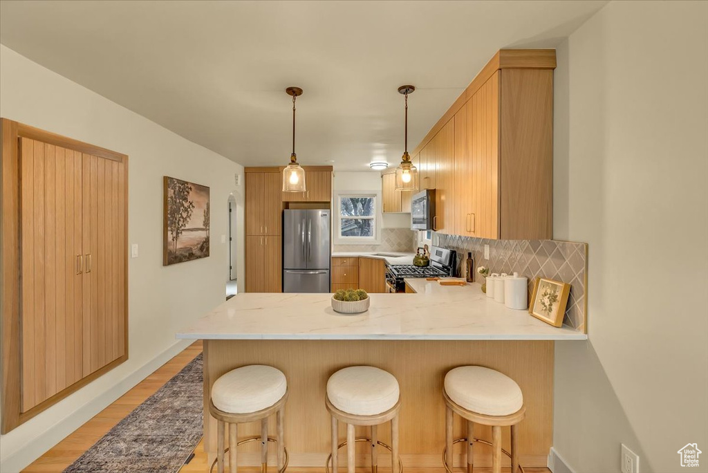 Kitchen featuring stainless steel appliances, a peninsula, backsplash, light wood-style flooring, and light countertops