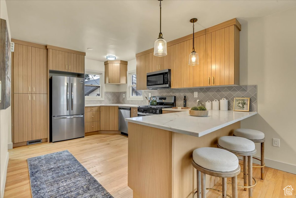 Kitchen with stainless steel appliances, a peninsula, a kitchen breakfast bar, pendant lighting, and tasteful backsplash
