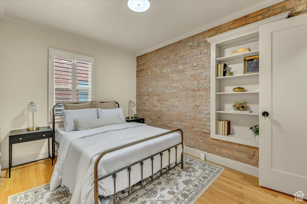 Bedroom featuring brick wall, crown molding, and wood finished floors