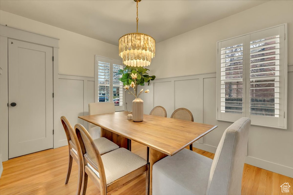 Dining space featuring a chandelier, a decorative wall, a wainscoted wall, and light wood-type flooring