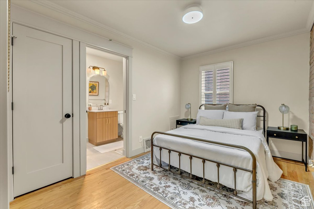 Bedroom with ornamental molding, light wood-type flooring, and ensuite bathroom