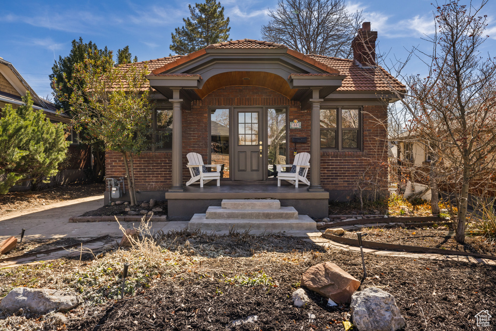 View of front of property with brick siding, a porch, a tile roof, and a chimney