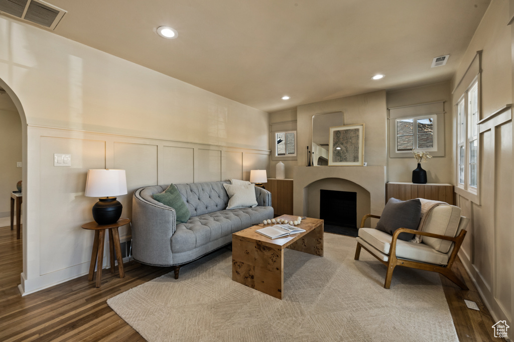 Living area with a decorative wall, arched walkways, wood finished floors, recessed lighting, and a wainscoted wall