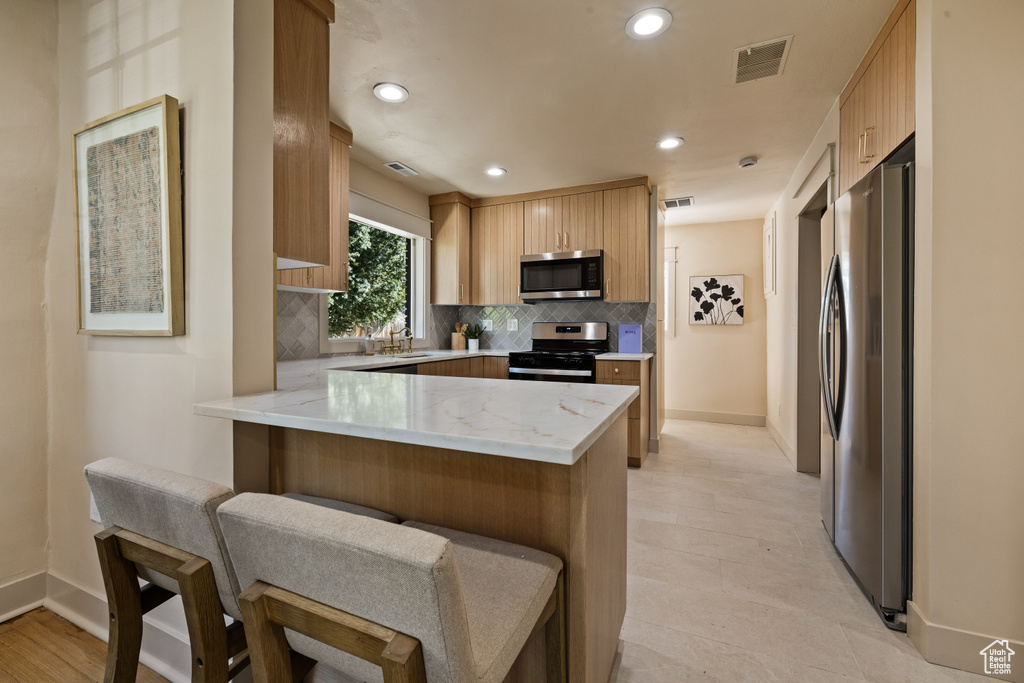 Kitchen with appliances with stainless steel finishes, a peninsula, tasteful backsplash, light stone countertops, and a breakfast bar
