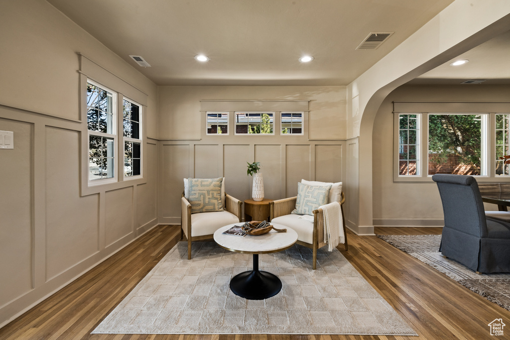 Living area with a decorative wall, wood finished floors, plenty of natural light, arched walkways, and recessed lighting