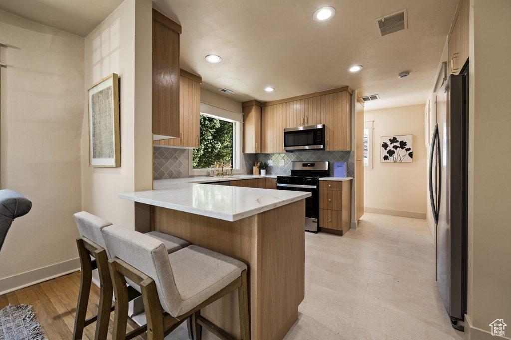 Kitchen featuring stainless steel appliances, a peninsula, backsplash, a breakfast bar area, and recessed lighting