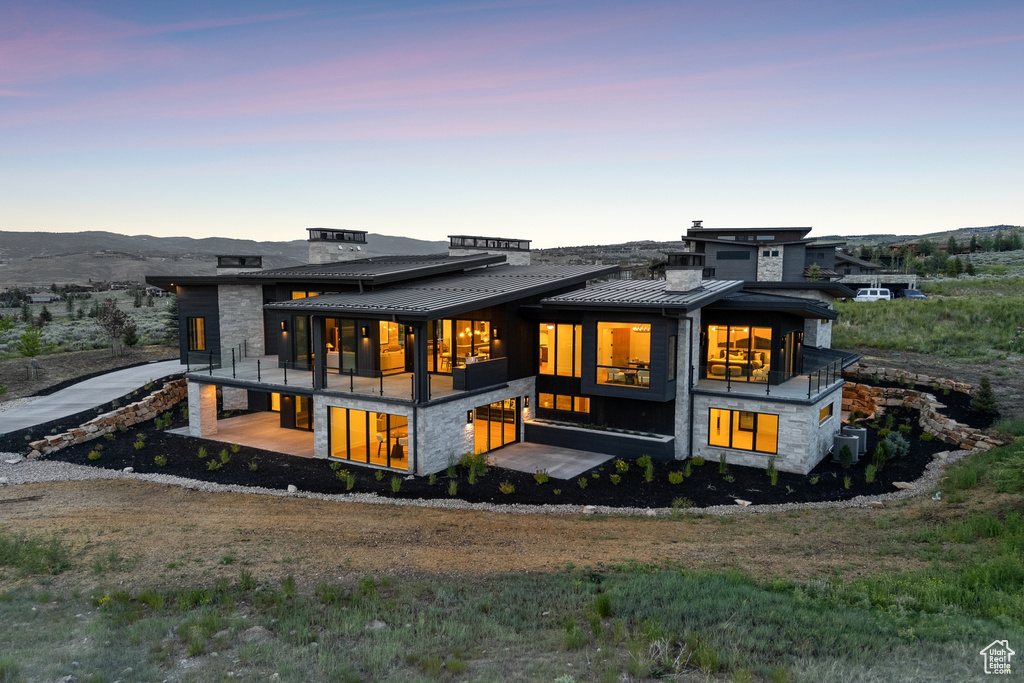 Back of property at dusk with a standing seam roof, a balcony, a metal roof, and stone siding