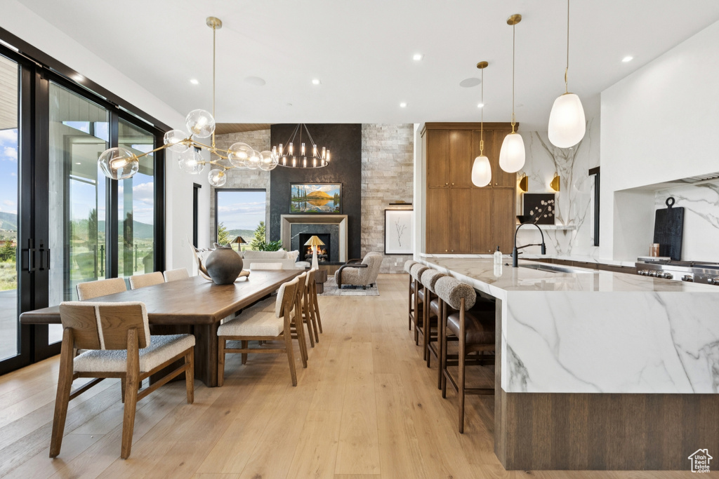 Dining space with light wood finished floors, a warm lit fireplace, a chandelier, and recessed lighting