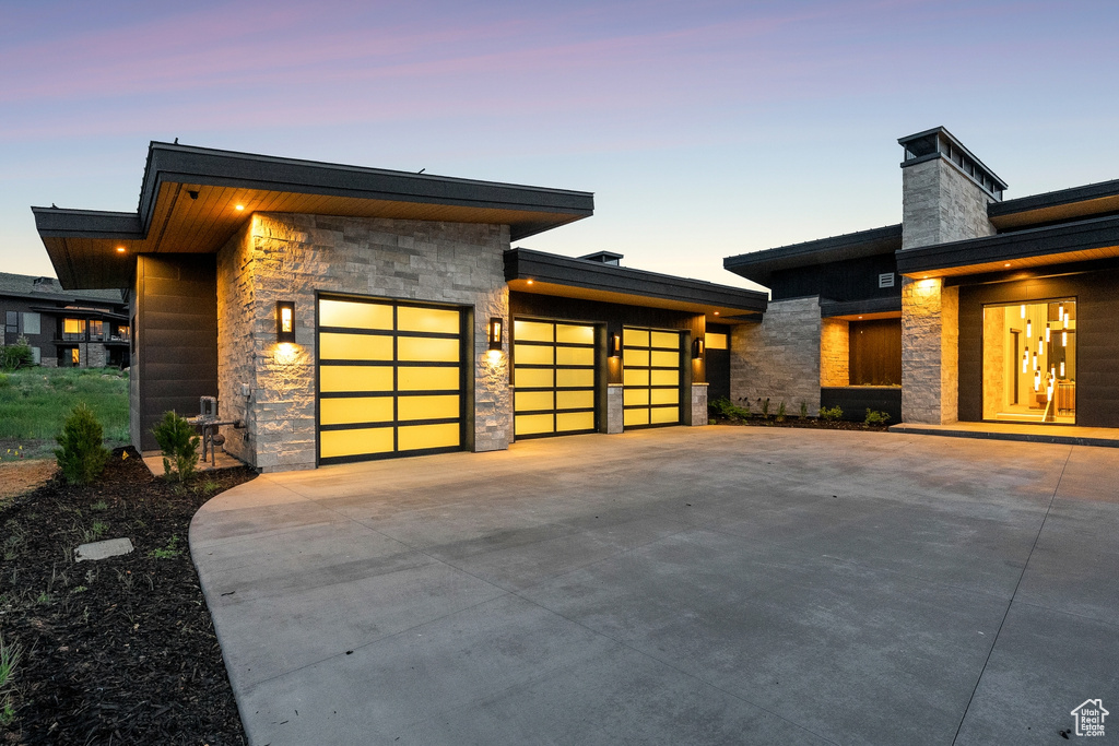 View of front facade with stone siding, a garage, concrete driveway, and a chimney
