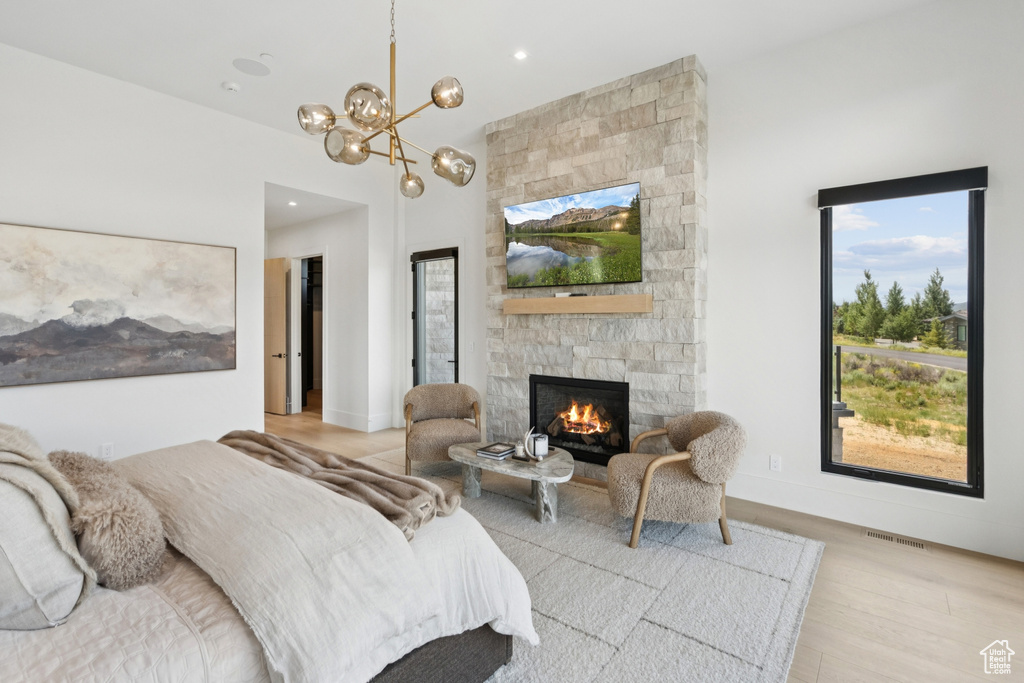 Bedroom featuring light wood finished floors, a stone fireplace, a chandelier, and recessed lighting