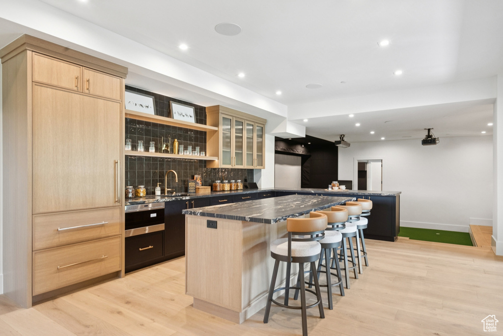 Kitchen featuring light brown cabinets, a breakfast bar area, decorative backsplash, a center island, and light wood-style flooring