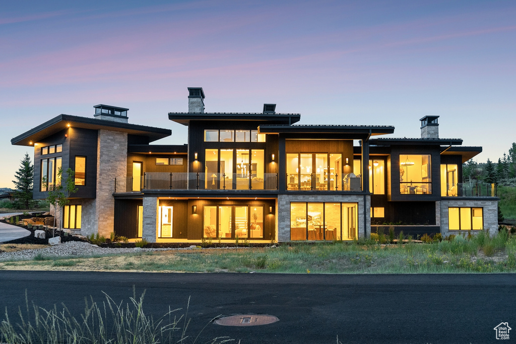 Back of property at dusk featuring a chimney and a balcony