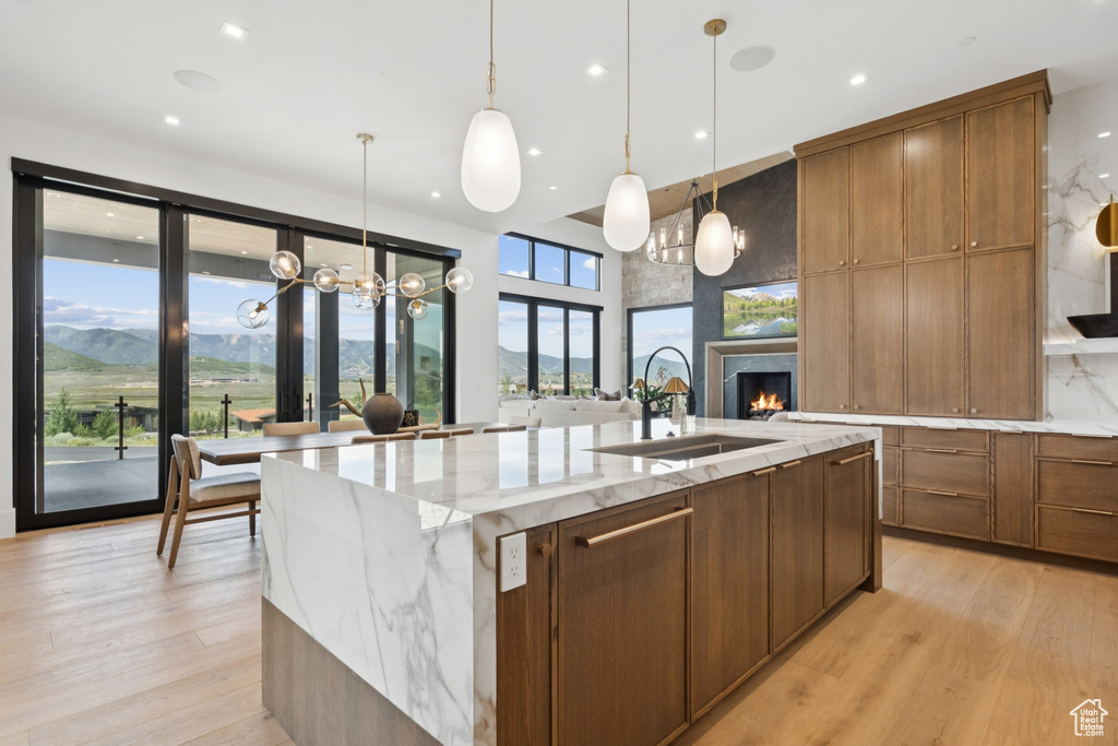 Kitchen with a fireplace, a large island, brown cabinets, light wood-style floors, and decorative light fixtures