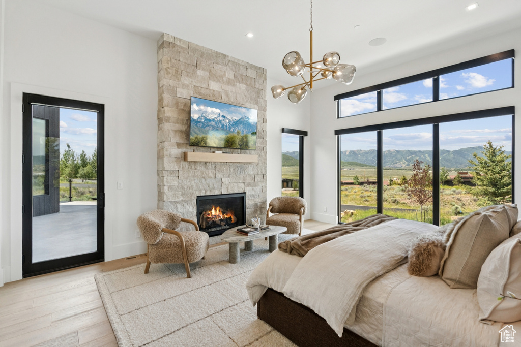 Bedroom featuring a towering ceiling, access to outside, a fireplace, light wood-type flooring, and a chandelier
