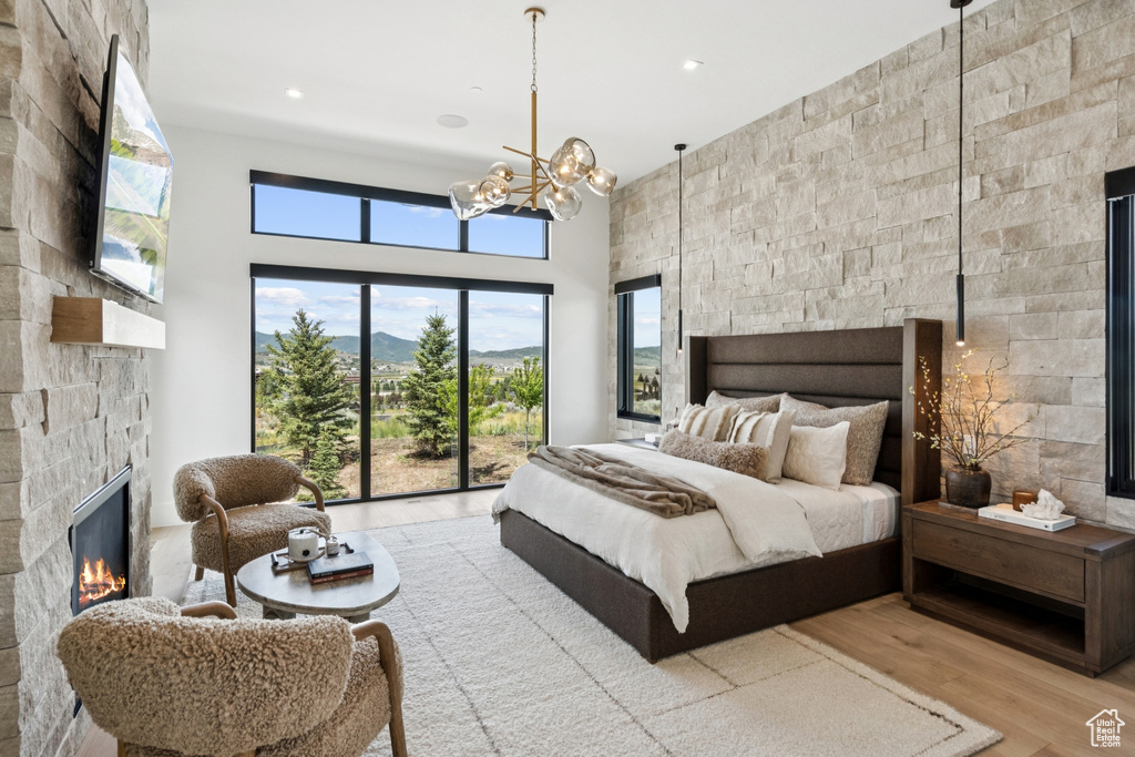 Bedroom with a fireplace, access to outside, wood finished floors, a chandelier, and a high ceiling