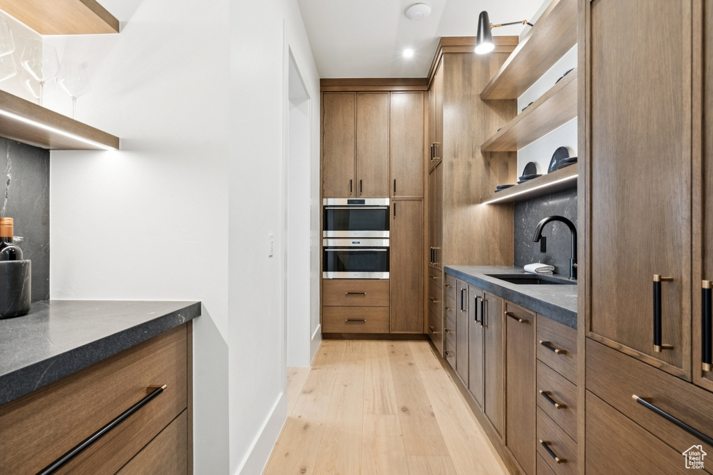Kitchen with open shelves, light wood-style flooring, double oven, and brown cabinets