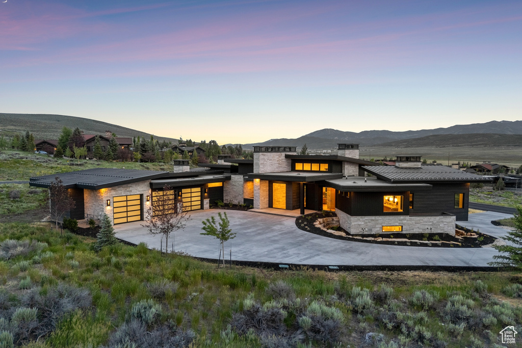 Back of house at dusk with stone siding, a mountain view, concrete driveway, and a metal roof