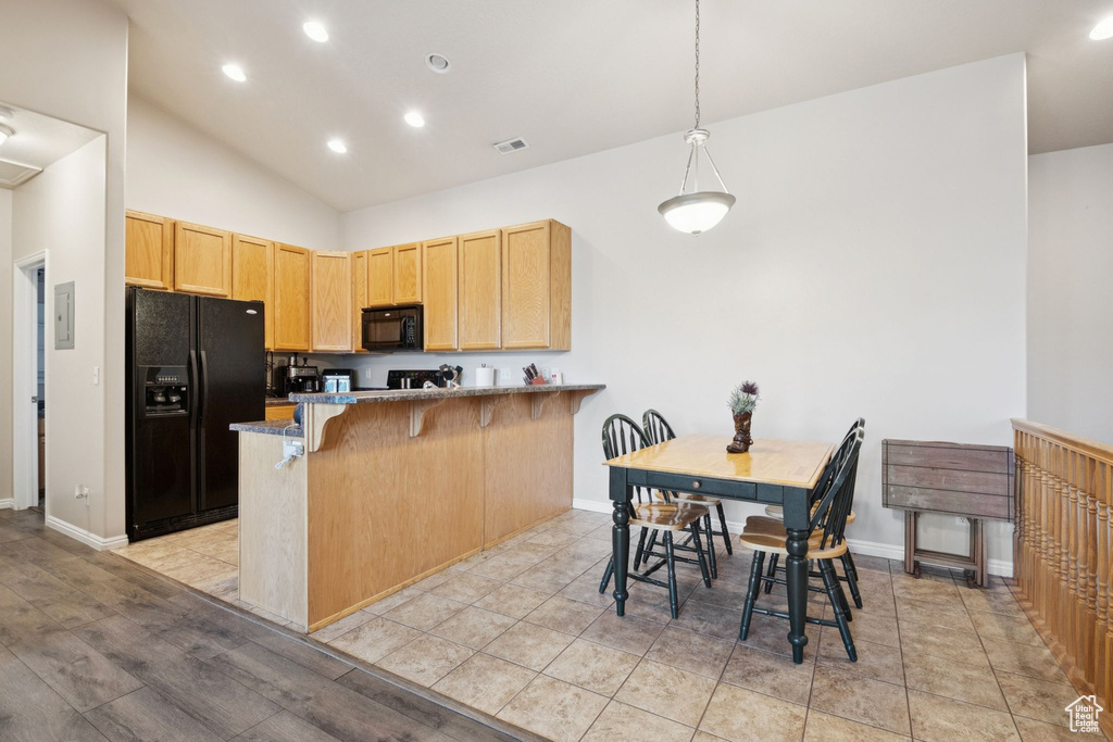 Kitchen featuring black appliances, a peninsula, a breakfast bar area, vaulted ceiling, and recessed lighting