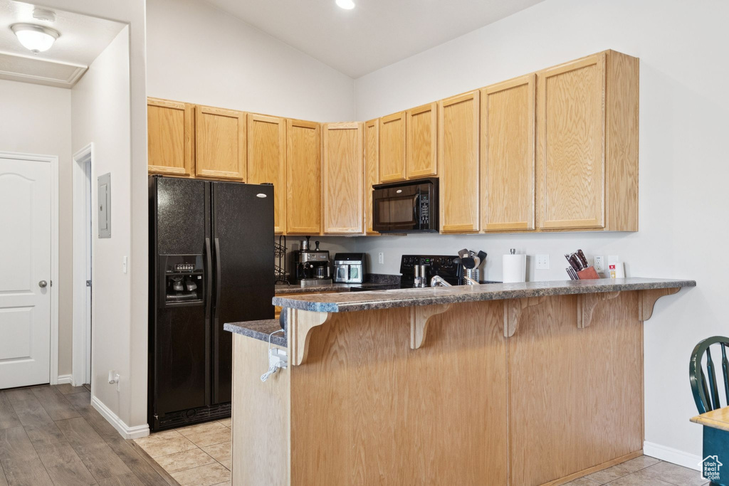 Kitchen featuring black appliances, a breakfast bar, dark countertops, a peninsula, and light brown cabinetry