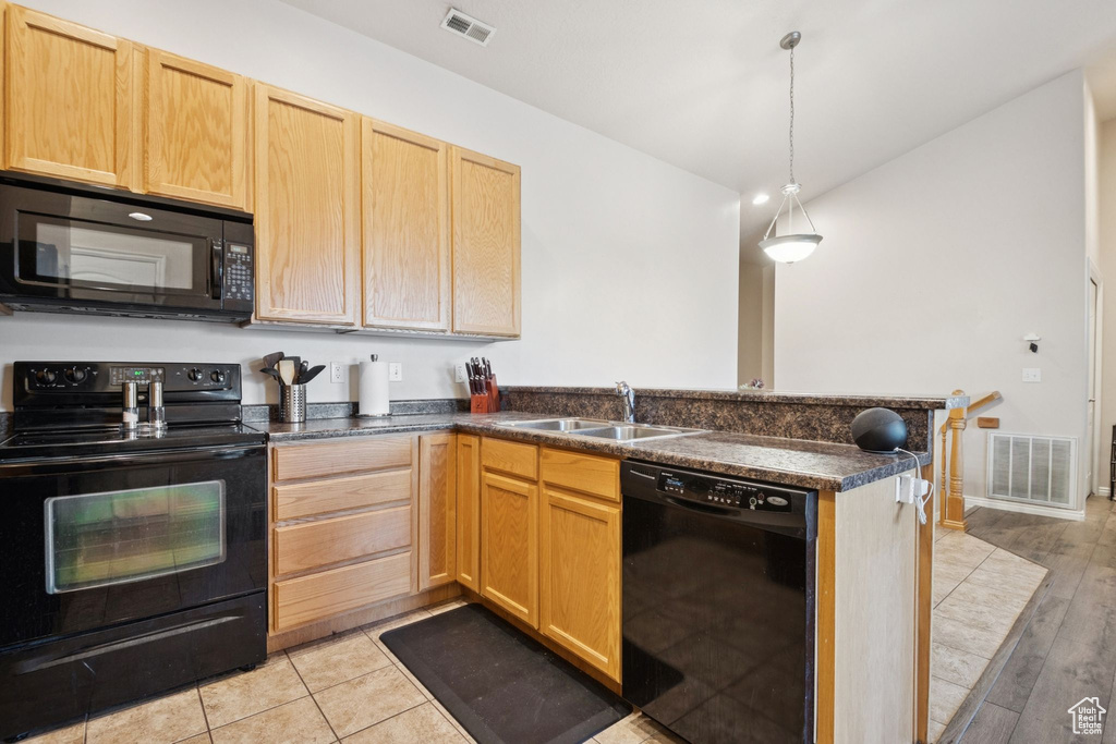 Kitchen with black appliances, a peninsula, dark countertops, and light brown cabinetry