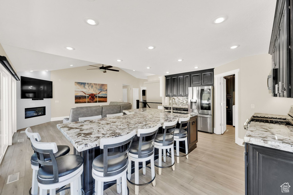 Kitchen with stainless steel appliances, light wood-style flooring, a breakfast bar, a glass covered fireplace, and recessed lighting
