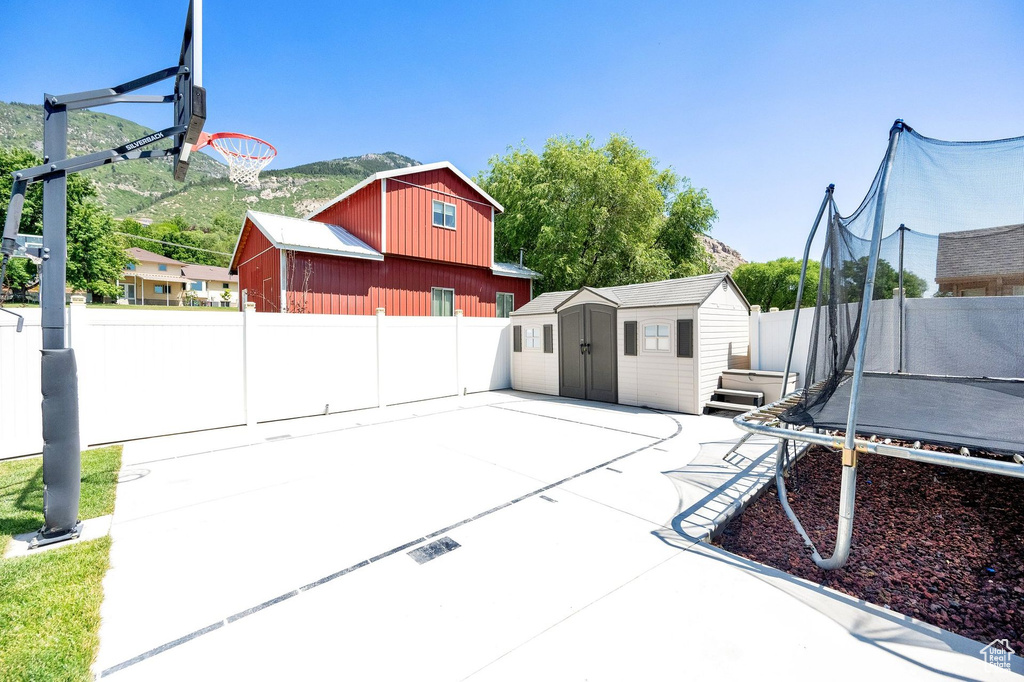 Fenced backyard featuring a trampoline, a shed, and a patio area