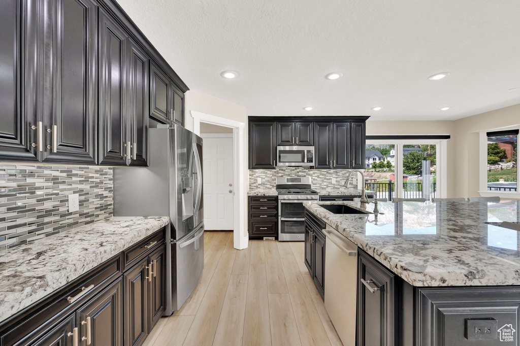 Kitchen featuring appliances with stainless steel finishes, backsplash, light wood finished floors, light stone countertops, and recessed lighting