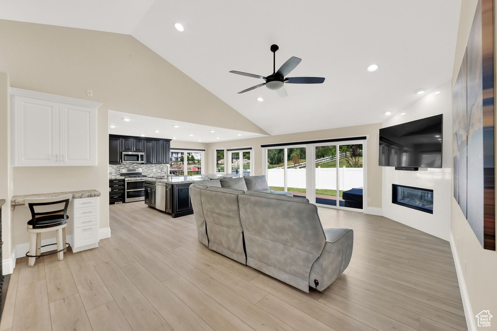 Living room featuring a large fireplace, ceiling fan, high vaulted ceiling, light wood-style flooring, and recessed lighting