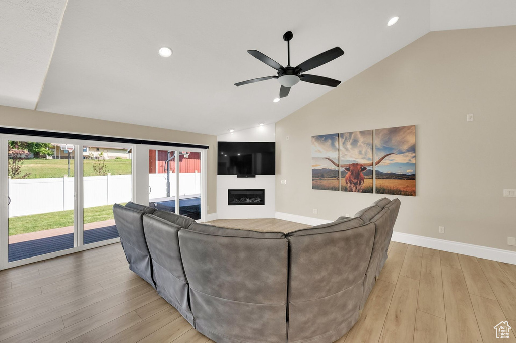Living room featuring vaulted ceiling, light wood-style flooring, a ceiling fan, recessed lighting, and a glass covered fireplace