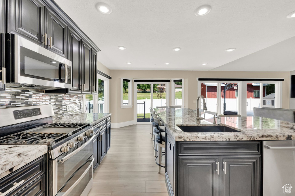 Kitchen with stainless steel appliances, backsplash, light wood-style floors, recessed lighting, and light stone counters