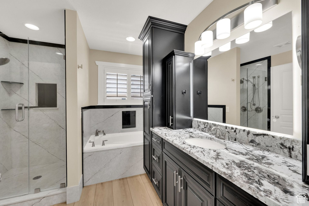 Bathroom with a garden tub, vanity, a marble finish shower, and wood finished floors