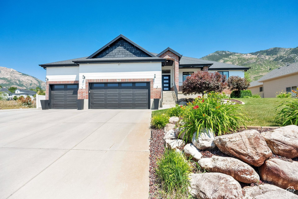 View of front of property with a mountain view, an attached garage, brick siding, concrete driveway, and a front lawn