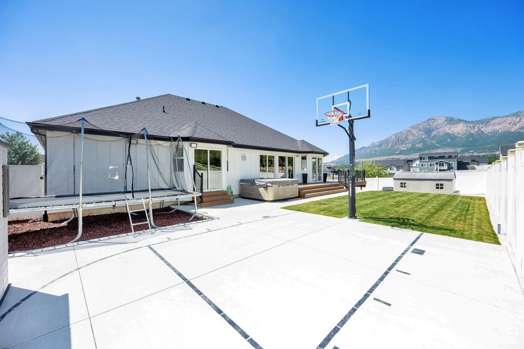 Rear view of house with a hot tub, a patio, a trampoline, a mountain view, and a shingled roof