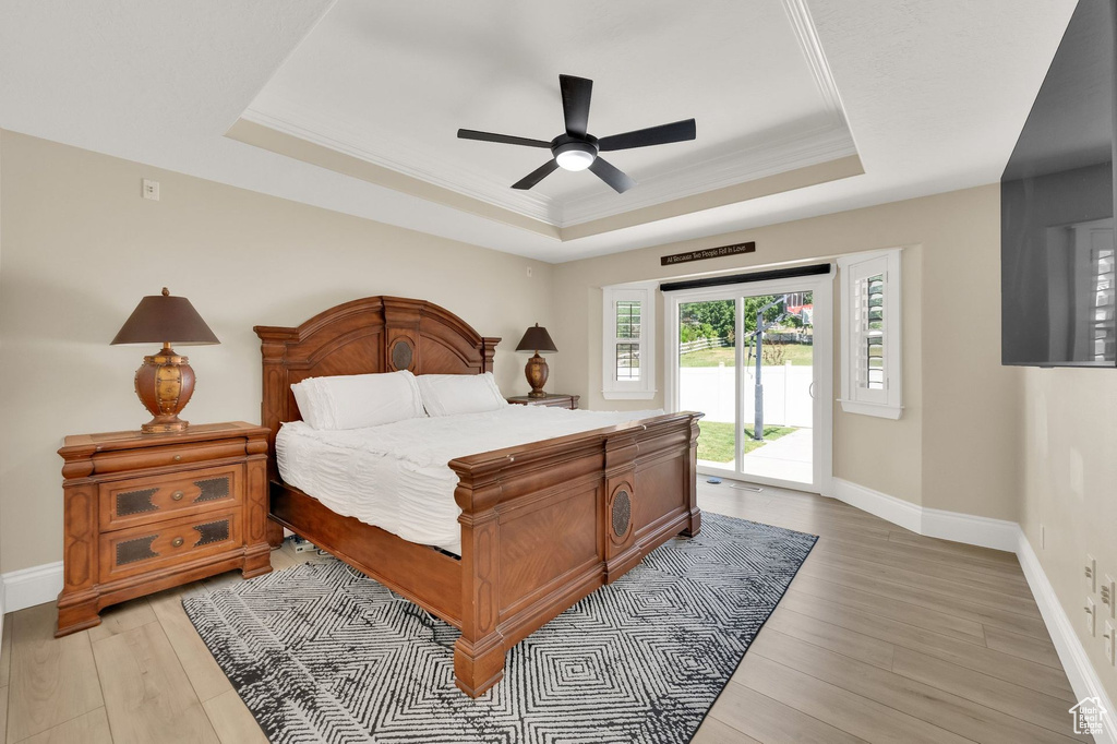 Bedroom with a tray ceiling, access to exterior, light wood-style flooring, ornamental molding, and a ceiling fan