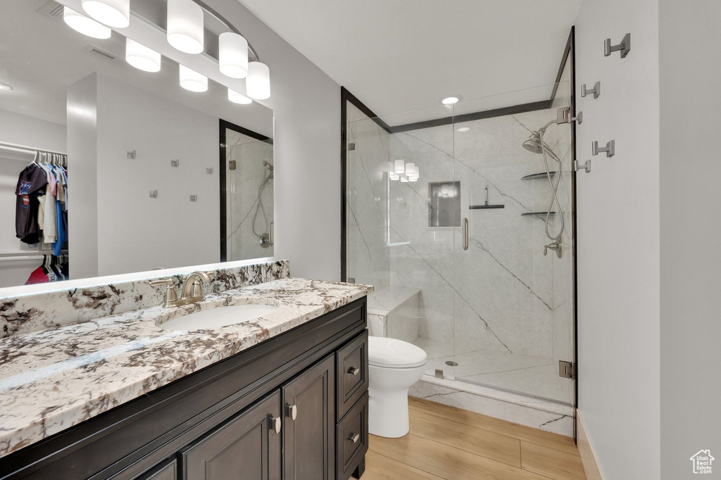 Full bath with vanity, a marble finish shower, wood finished floors, a spacious closet, and recessed lighting