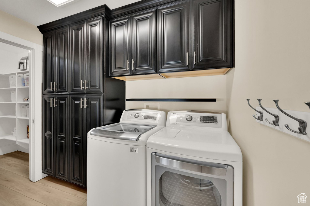 Washroom with cabinet space, independent washer and dryer, and light wood-style flooring