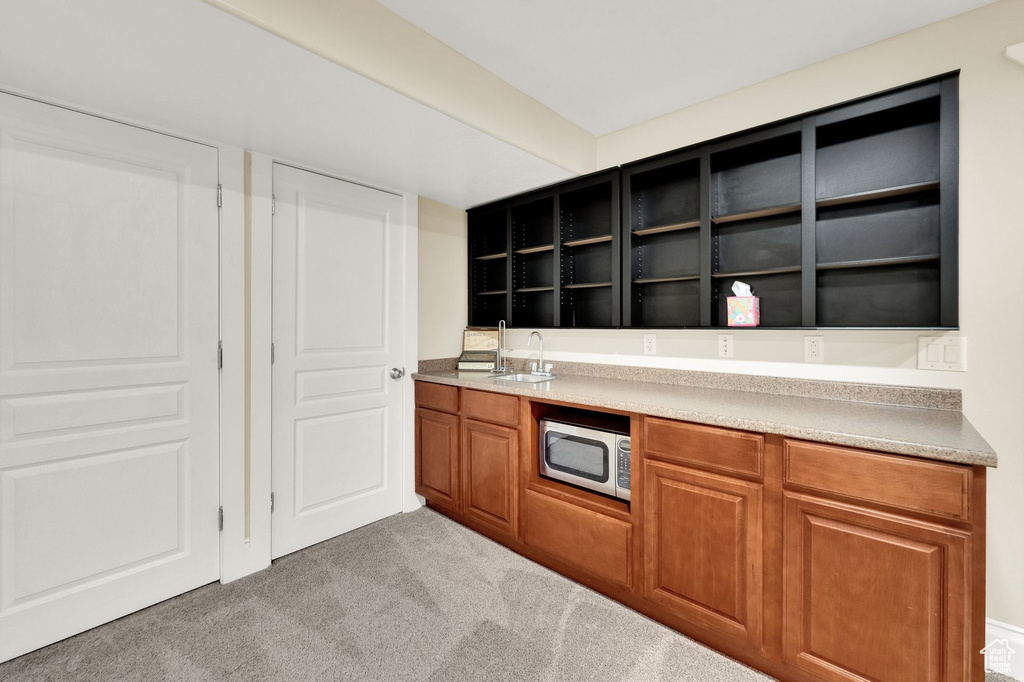 Kitchen with stainless steel microwave, light colored carpet, open shelves, brown cabinetry, and light countertops