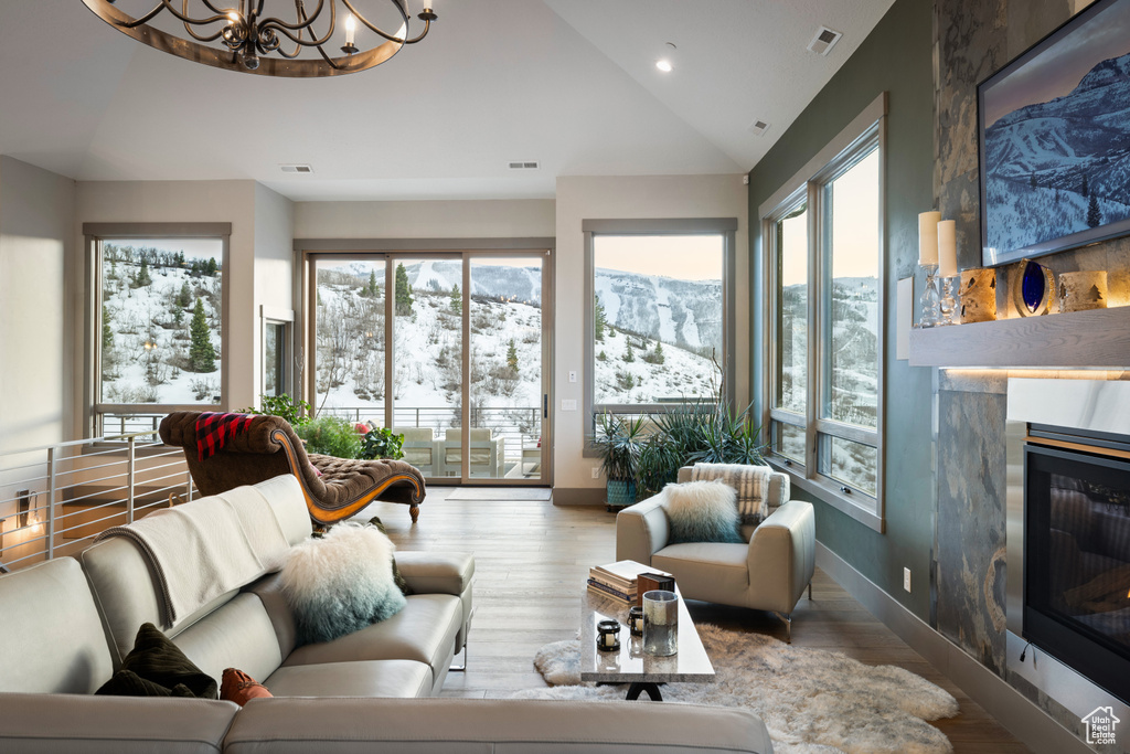 Living area with lofted ceiling, a glass covered fireplace, plenty of natural light, a chandelier, and wood finished floors