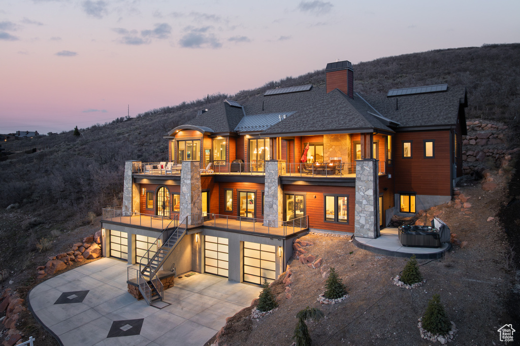 Rear view of house featuring a balcony, french doors, a chimney, concrete driveway, and an attached garage
