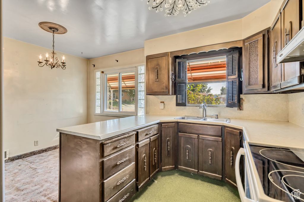 Kitchen with a chandelier, electric stove, a peninsula, light countertops, and decorative backsplash