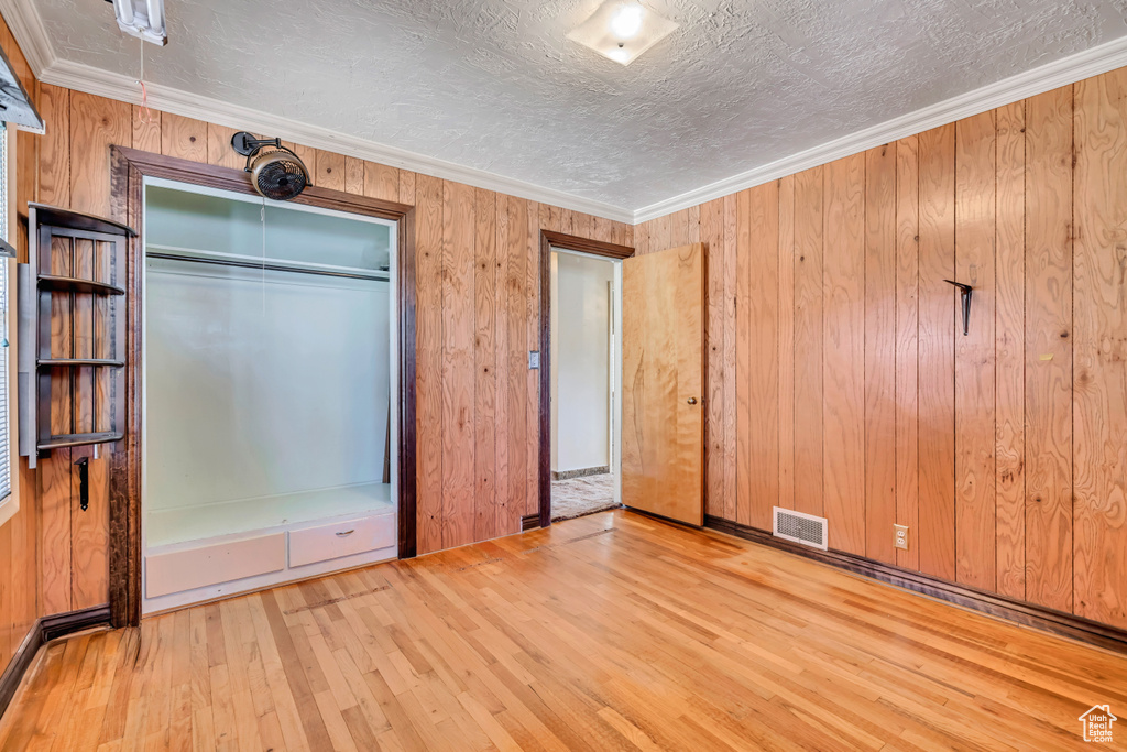 Unfurnished bedroom featuring hardwood / wood-style flooring, wood walls, ornamental molding, a closet, and a textured ceiling