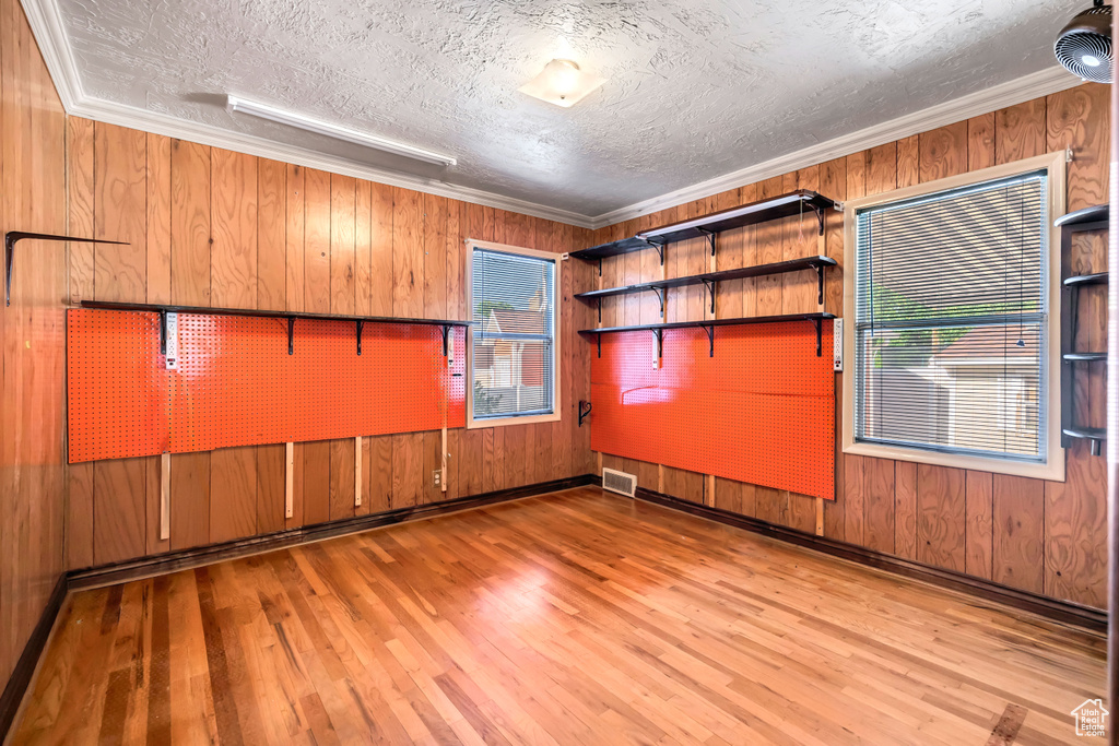 Unfurnished room with healthy amount of natural light, wood finished floors, ornamental molding, wooden walls, and a textured ceiling