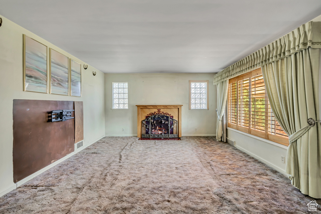 Unfurnished living room with carpet flooring and a warm lit fireplace