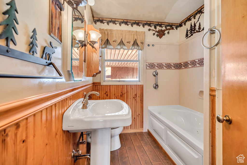 Full bathroom with wood walls, wood finished floors, and wainscoting