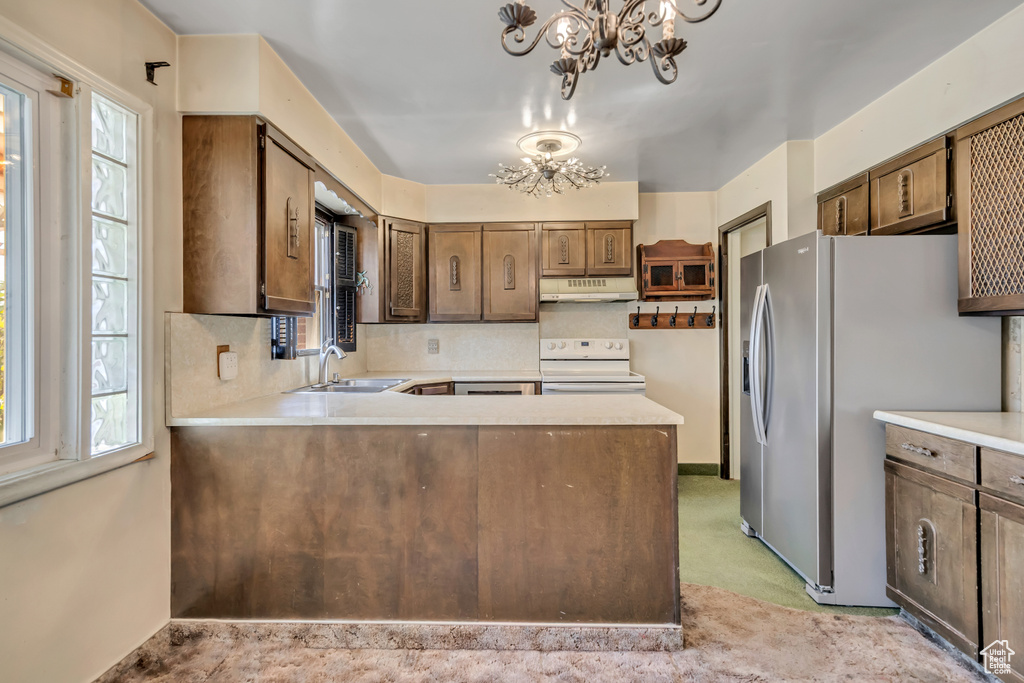 Kitchen featuring electric range, stainless steel fridge, a chandelier, under cabinet range hood, and light countertops