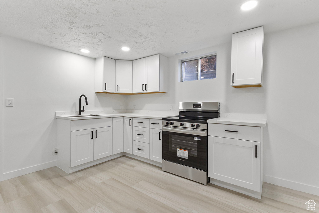 Kitchen featuring stainless steel range with electric stovetop, light countertops, white cabinetry, recessed lighting, and light wood finished floors