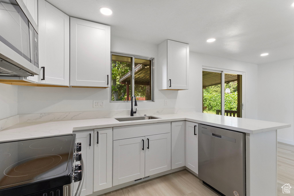 Kitchen with stainless steel appliances, light wood-style floors, white cabinets, a peninsula, and light stone countertops
