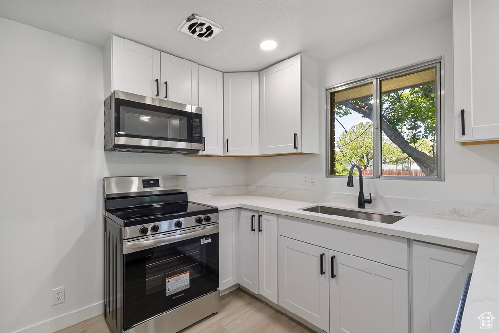 Kitchen with stainless steel appliances, white cabinetry, light wood-style floors, and recessed lighting