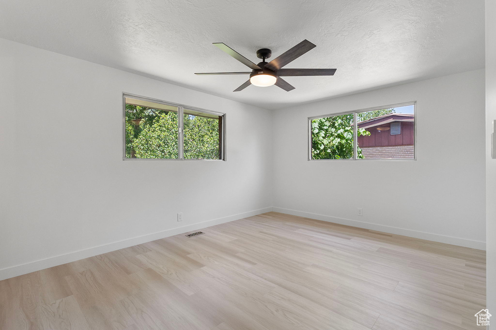 Spare room featuring healthy amount of natural light, a ceiling fan, light wood-type flooring, and a textured ceiling