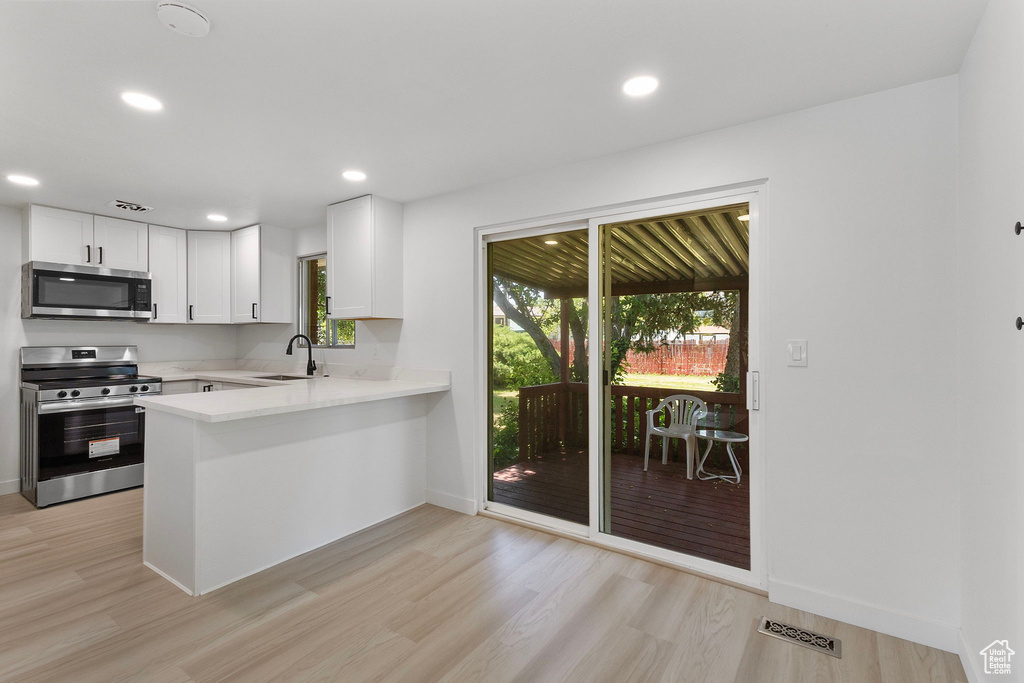 Kitchen featuring stainless steel appliances, light countertops, a peninsula, light wood-style floors, and recessed lighting